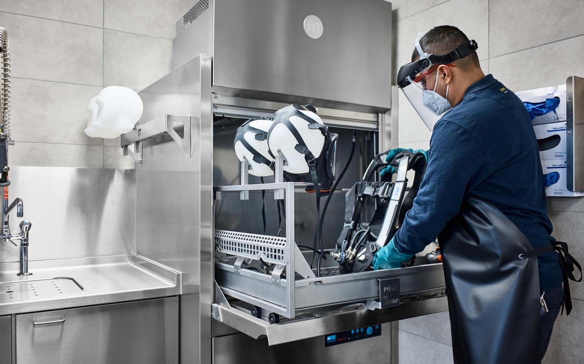 Gerätewart bestückt TopClean D mit Masken auf Maskenköpfe und setzt Trageplatte in den Korb